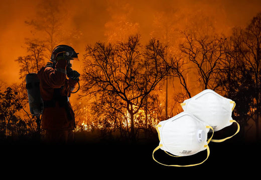 Image features two N95 respirators, on top of a photo of a firefighter working to contain a wildfire