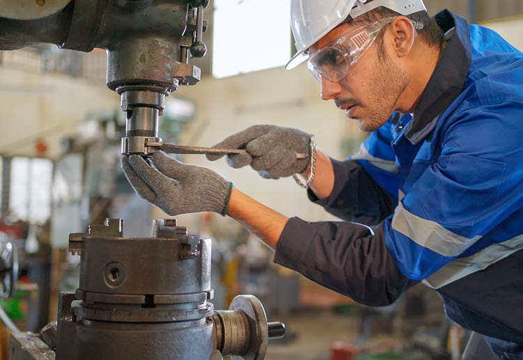 A man wearing safety glasses, work gloves and a protective helmet uses a wrench to tighten a piece of equipment